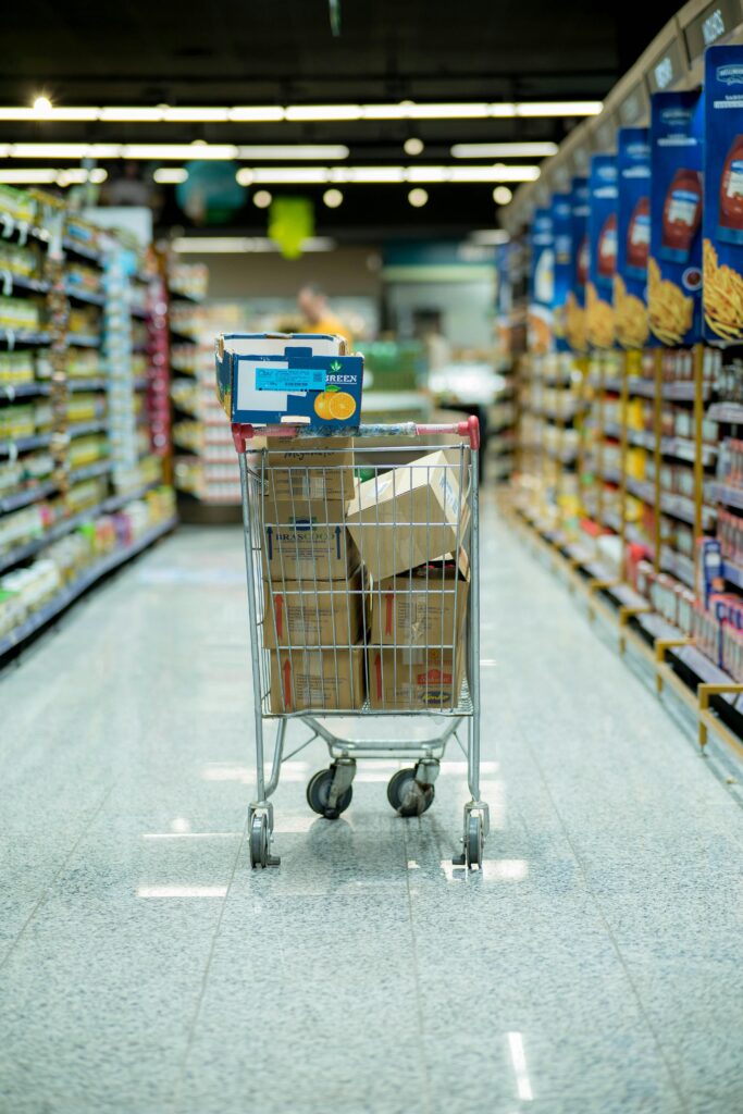 A shopping cart with packages in a grocery aisle, showcasing everyday shopping options.
